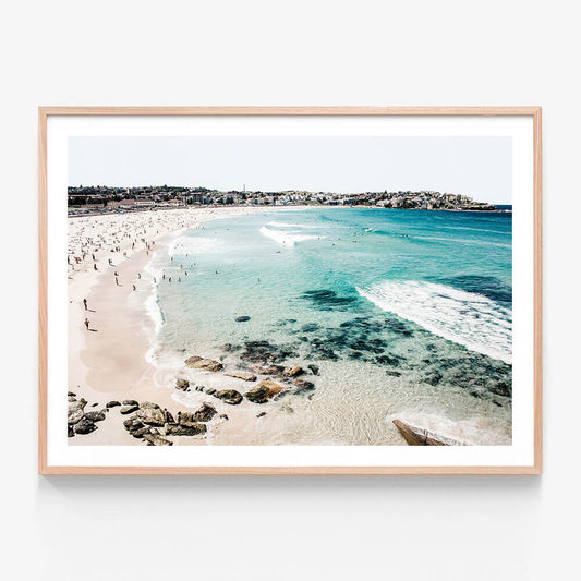 A framed print of Bondi Beach with clear blue water, sand, and a coastal landscape.