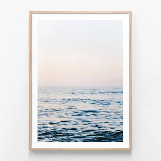 A framed print of a calm ocean with a minimalist design, featuring gentle waves and a soft blue coastal colour palette.