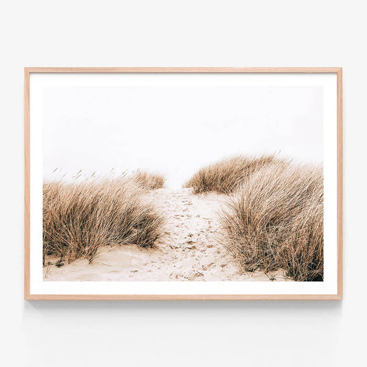A framed photo print of a sandy coastal path with tall grass on either side.