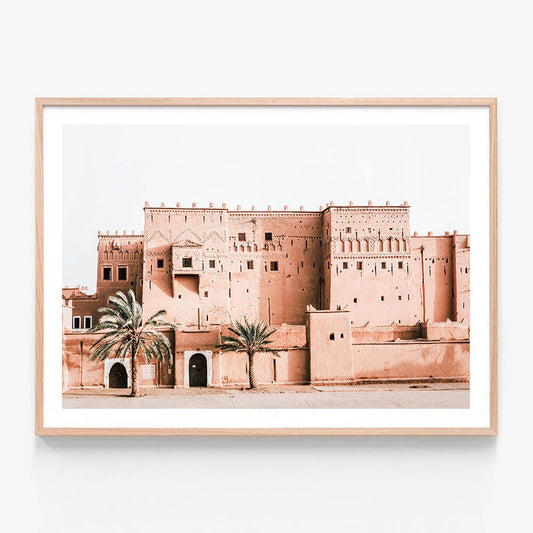 A framed photo print of a Moroccan Kasbah with walls and several gates or openings, surrounded by palm trees.