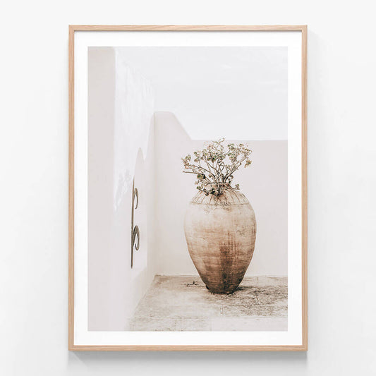 A framed artwork featuring a large earthenware vase with a dried plant arrangement, placed against a neutral background.