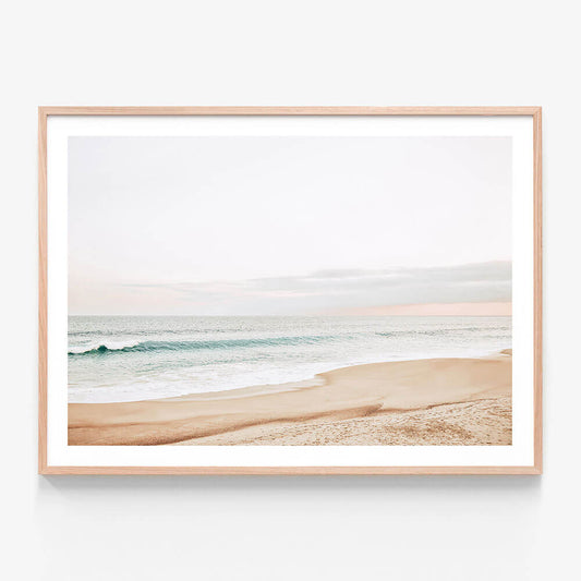 A pastel-colored photograph of a coastal scene with a beach and ocean waves in the background. Framed wall art print