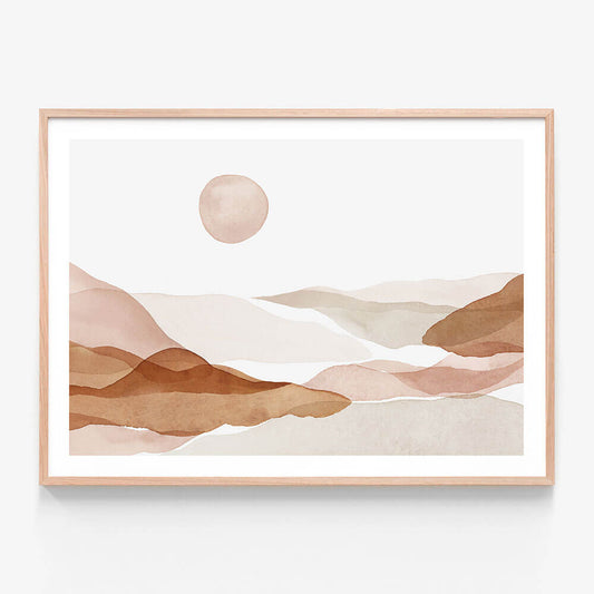 A framed art print of a watercolor painting of abstract hills in beige, brown, and white colors with a sun in the background.