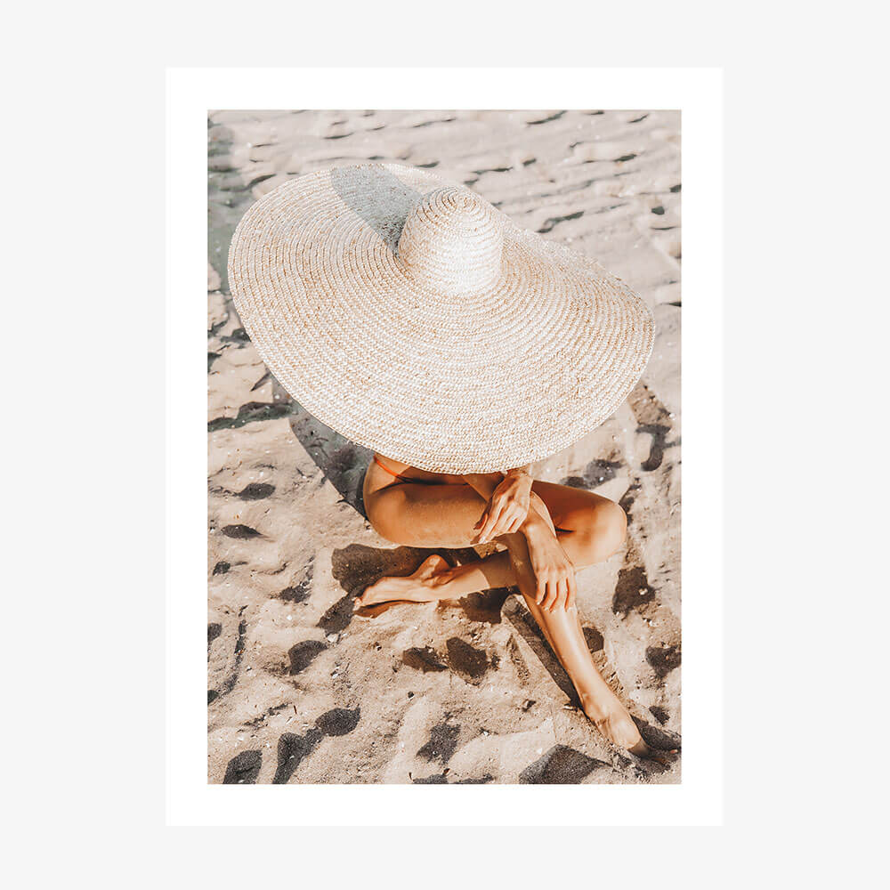 A photo wall art print featuring a woman on the beach wearing a Beach Hat in the sand