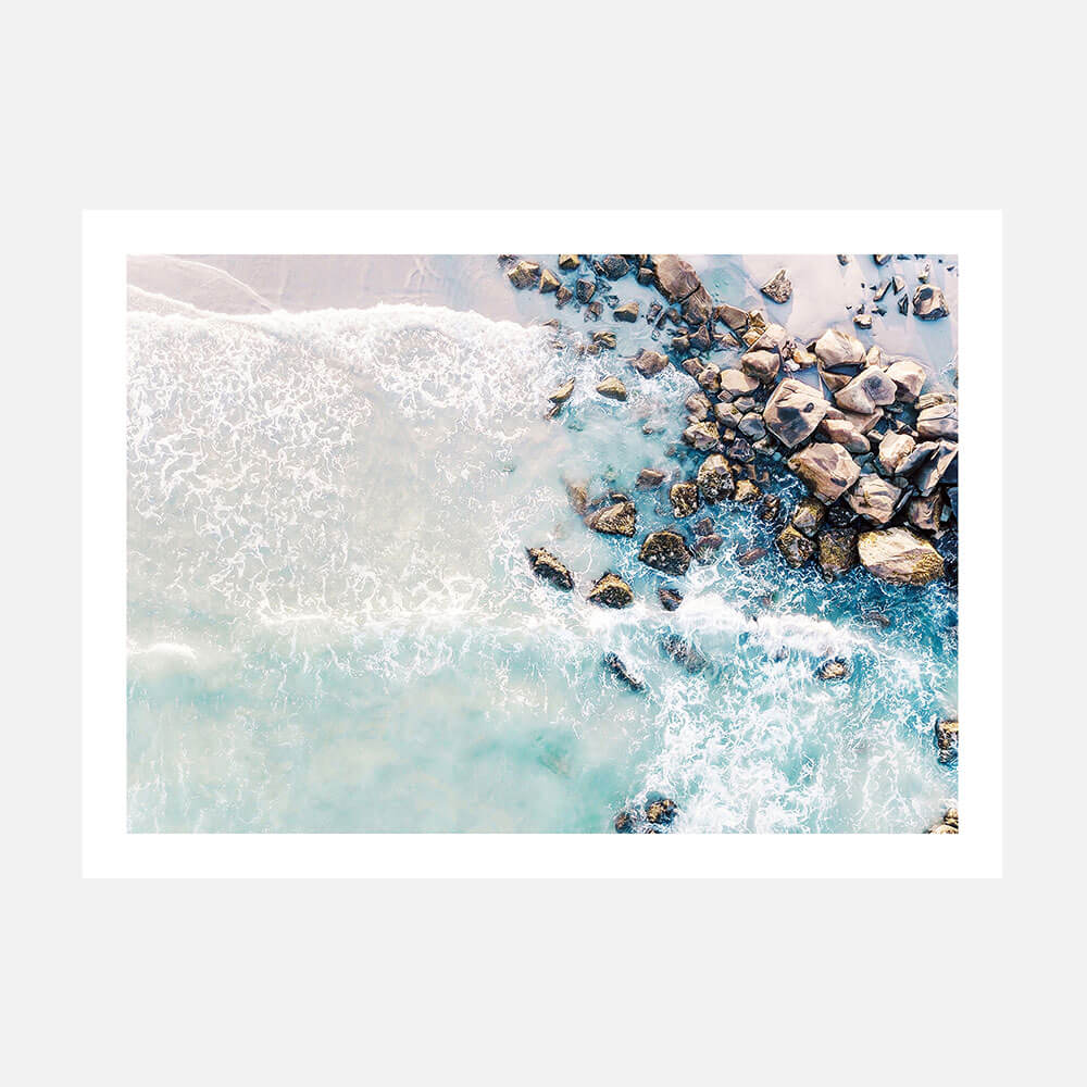 A coastal artwork print of a beach scene with rocks and waves in blue tones.