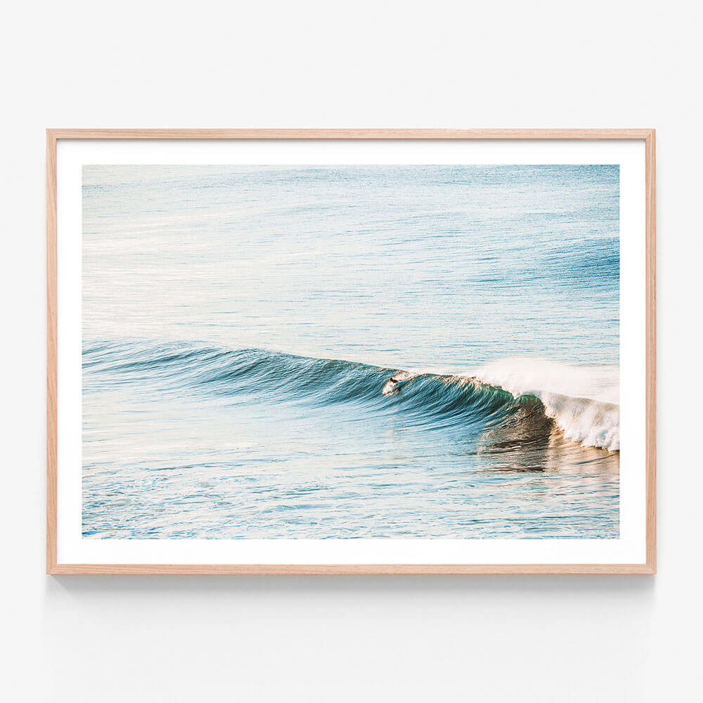 A photographic print featuring a surfboard on a gentle wave in the ocean at Bells beach, with a minimalist style and a blue and white color palette.