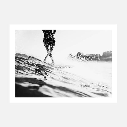 A photo wall art print featuring a black and white photo of a person surfing on a wave with a coastal background.