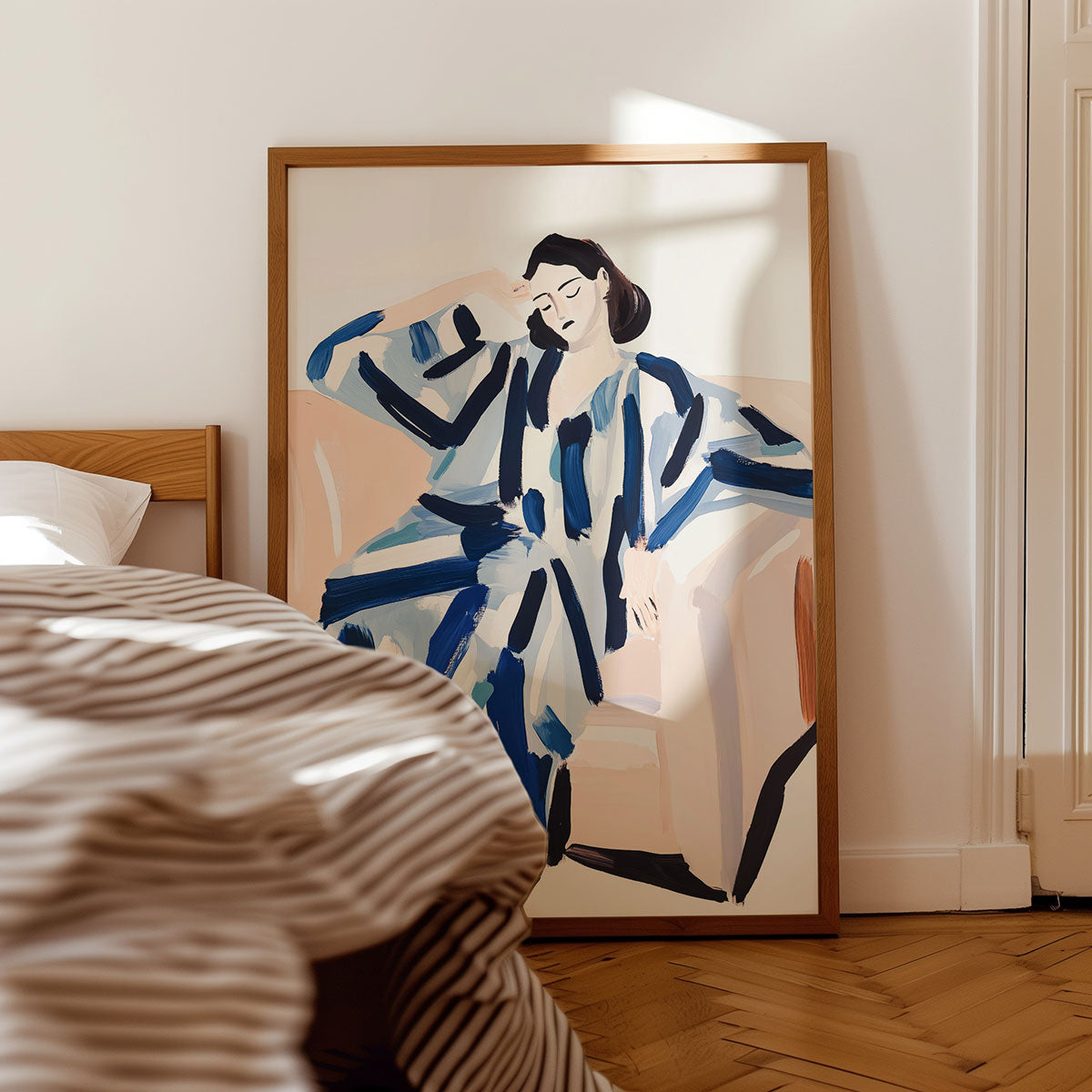 Framed artwork of a woman in a blue striped pyjamas on a wall above a bed.