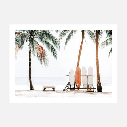 A photo art print featuring multiple surfboards leaning against a beach chair with palm trees in the background.