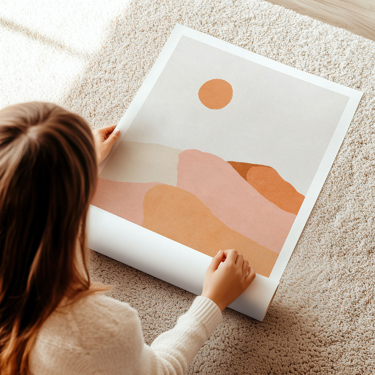 A woman unrolling a colourful boho art print on a carpeted floor.