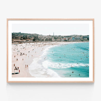 A framed print of Bondi Beach, showing the beach filled with people and the ocean with waves.