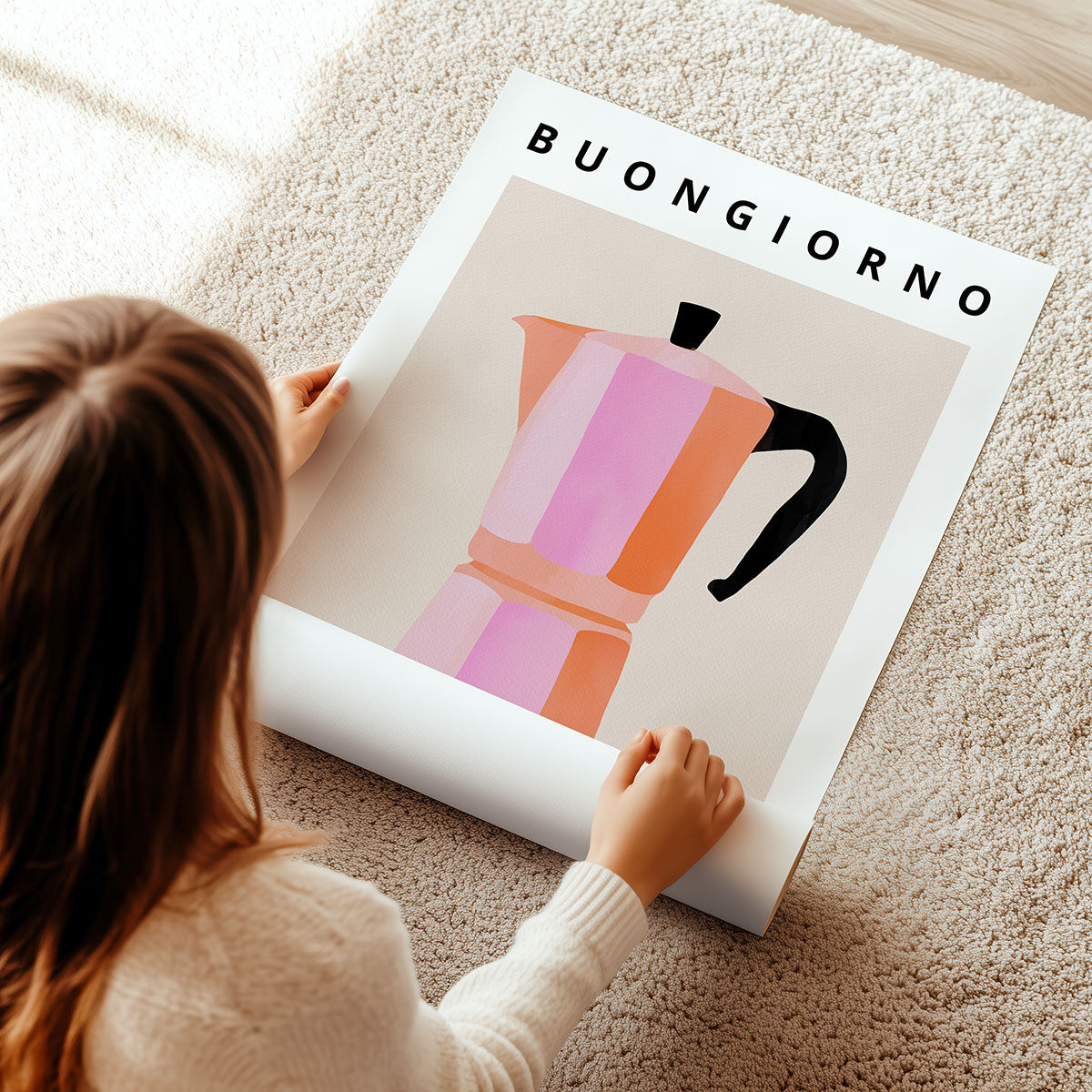 Person unrolling a poster print with a colourful coffee pot design and 'BUONGIORNO' text on a carpeted floor.