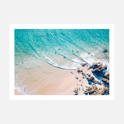 An overhead photograph print of The Pass beach with clear blue water, brown sand, and rocks, likely taken in Byron Bay, Australia.