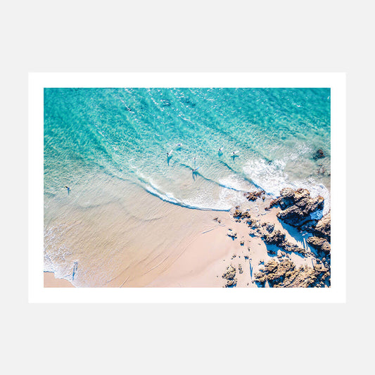 An overhead photograph print of The Pass beach with clear blue water, brown sand, and rocks, likely taken in Byron Bay, Australia.