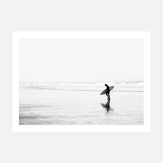 A poster print of a black and white photo of a surfer walking along the beach.