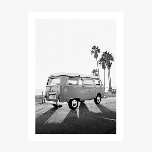 This poster print features a black and white photograph titled "Cali Van," showcasing a classic black and white image of a Volkswagen Type 2 van, commonly known as a "Kombi." The scene is set in a serene, sunlit environment with palm trees in the background, enhancing the iconic and idyllic vibe of the picture.