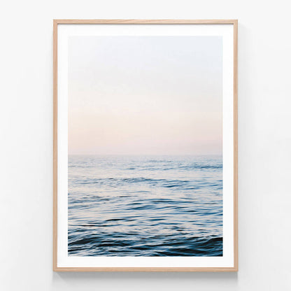 A framed print of a calm ocean with a minimalist design, featuring gentle waves and a soft blue coastal colour palette.