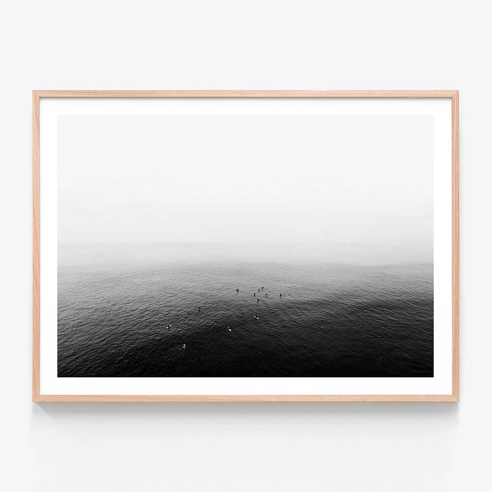 A framed art print of a black and white photo of a calm ocean with a few people in the distance.