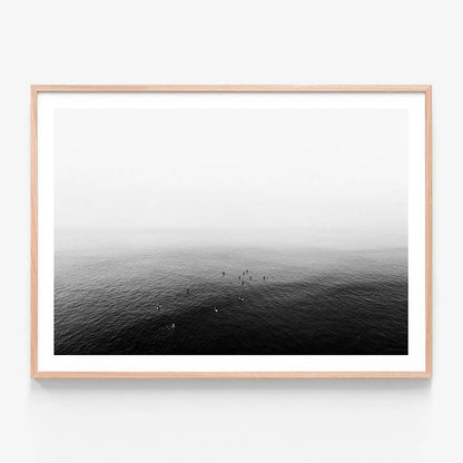A framed art print of a black and white photo of a calm ocean with a few people in the distance.