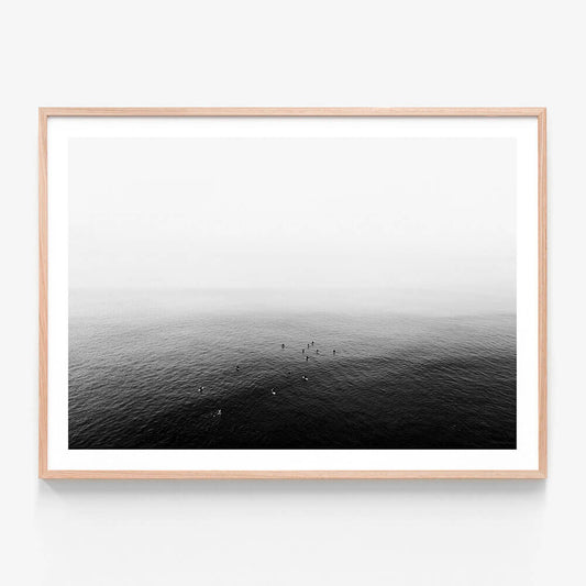 A framed art print of a black and white photo of a calm ocean with a few people in the distance.