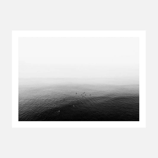 A black and white photo of a calm ocean with a few people in the distance.