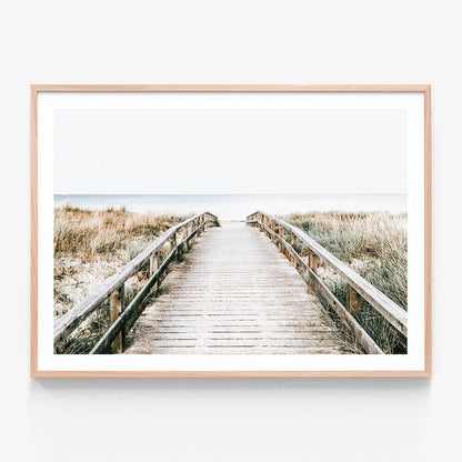 A print of a coastal boardwalk leading towards the ocean, with a bright sky and grassy dunes on either side.