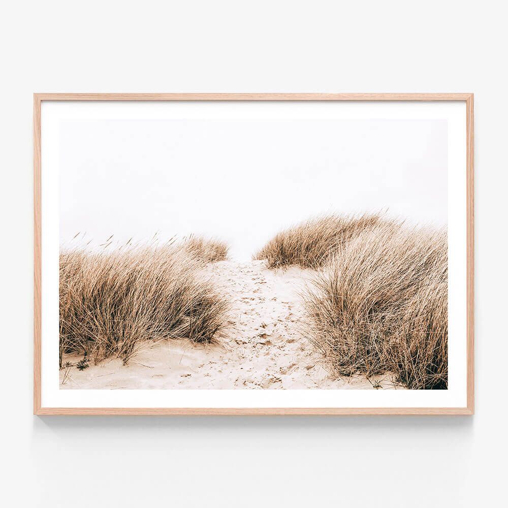 A framed photo print of a sandy coastal path with tall grass on either side.