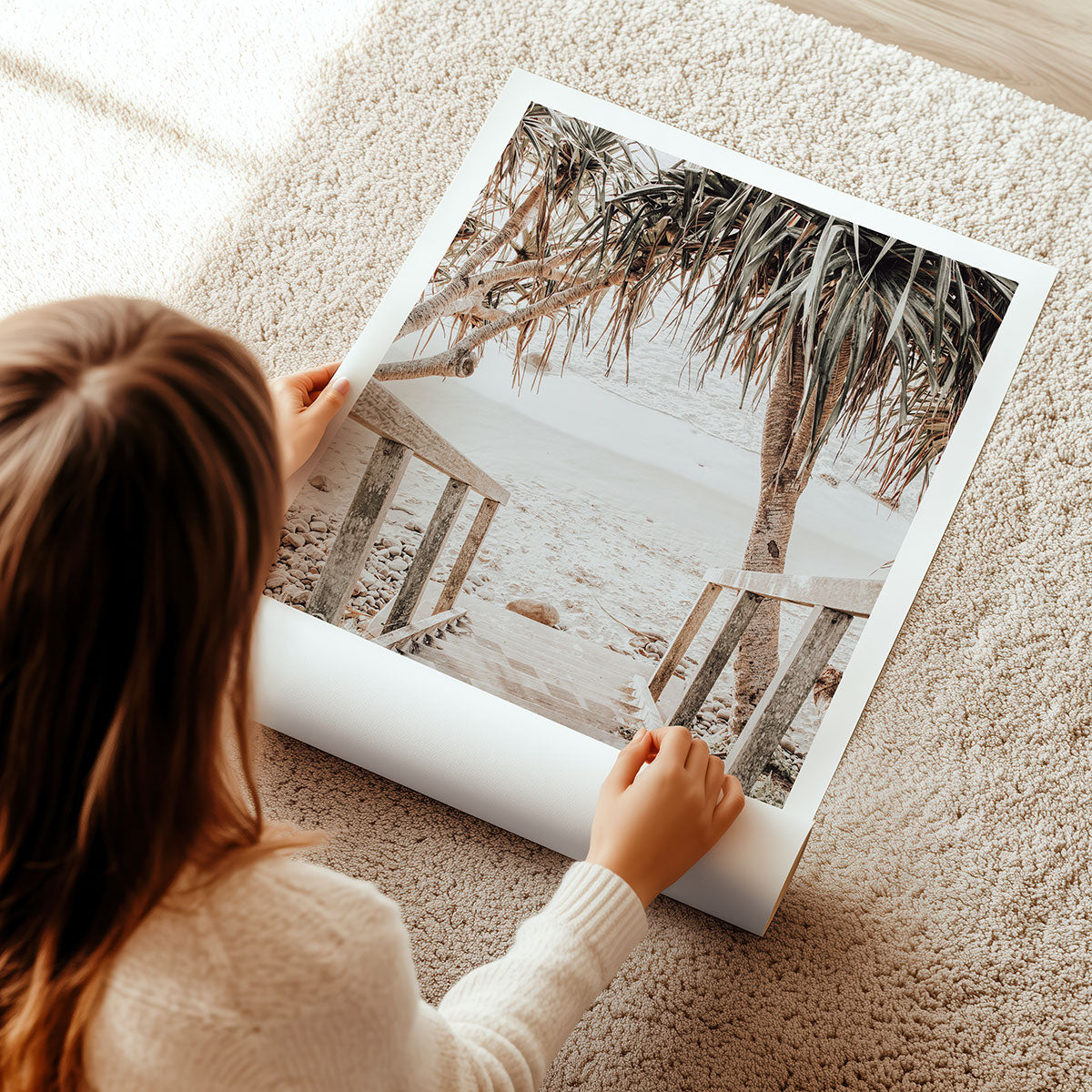 Woman unrolling a large poster print of a coastal beach scene on a carpeted floor