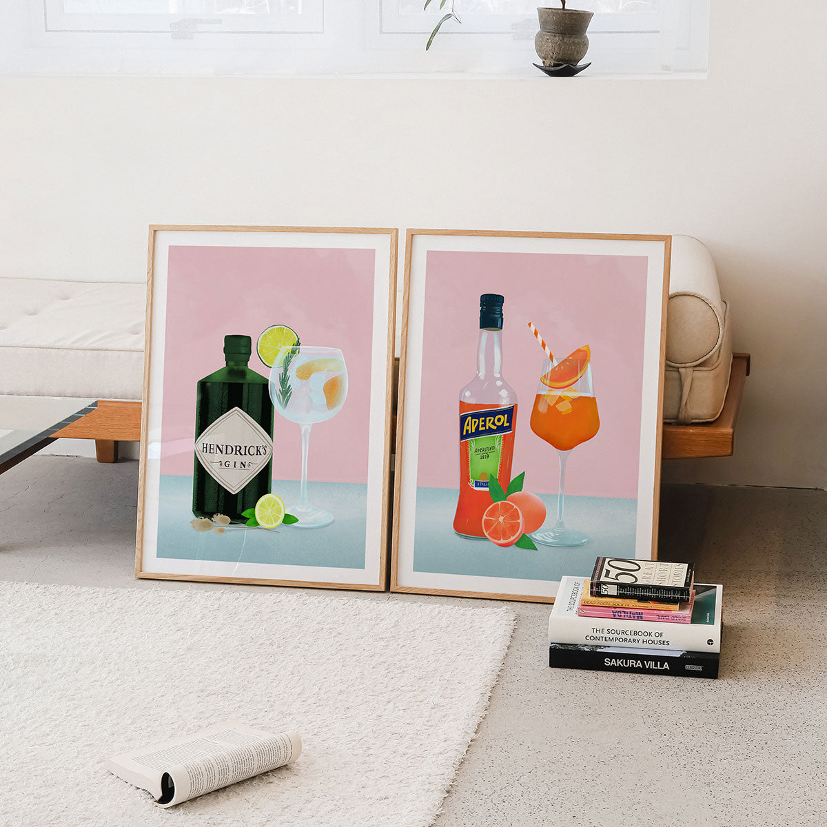 Two framed Wall art prints of cocktail posters on a wall with books below.