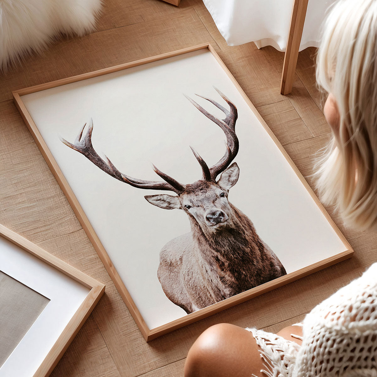 Framed art picture of a deer on a wooden floor with a person sitting nearby.