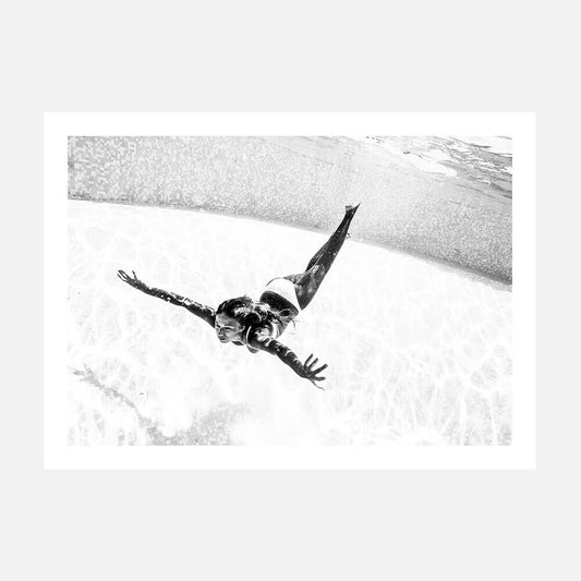 Black and white photography print of a girl swimming underwater in a pool. 