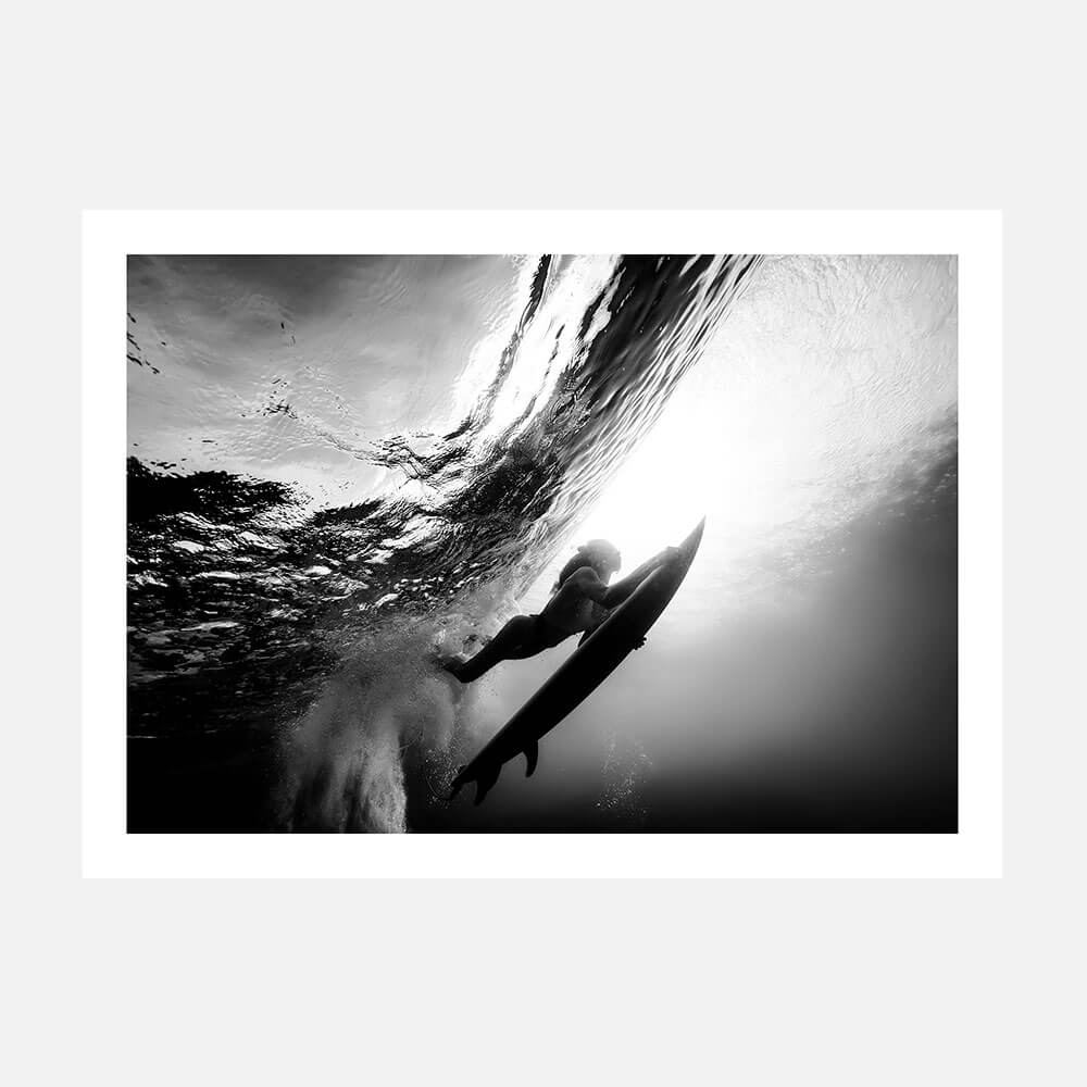 Black and white photography print of a female surfer duck diving under a wave.