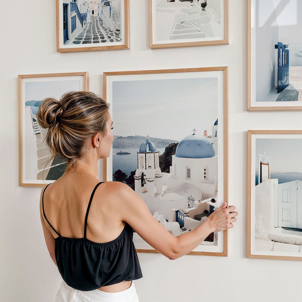 Woman arranging framed art prints on a wall. They are all photography print from Europe, Santorini in Greece.