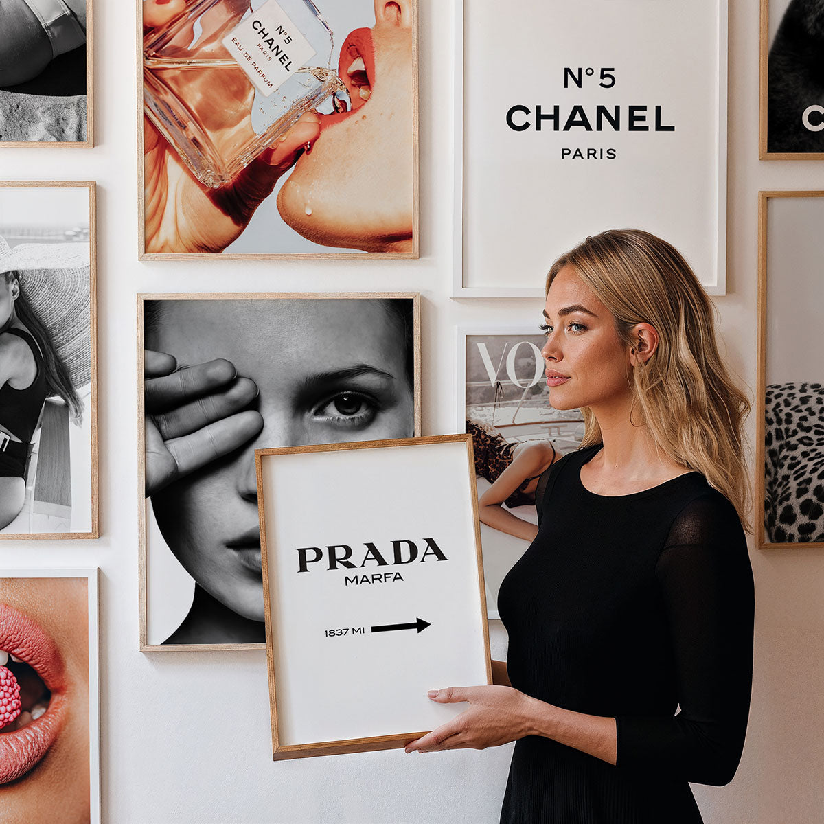 Woman holding a framed picture with 'Prada' text against a gallery wall of framed art and fashion images.