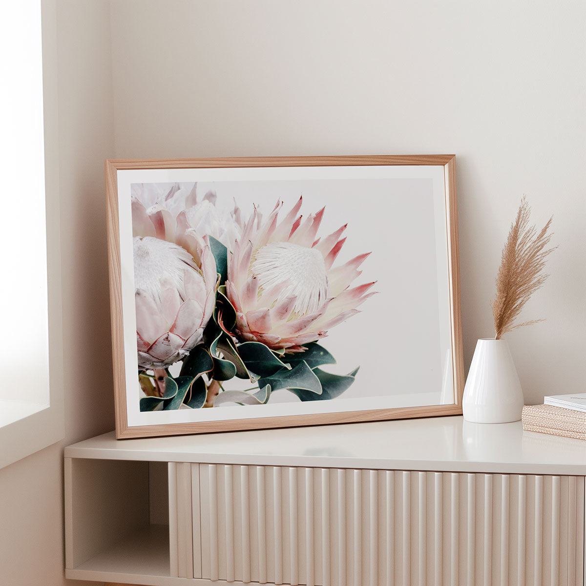 Framed floral artwork on a shelf with a vase and books in a minimalistic room.