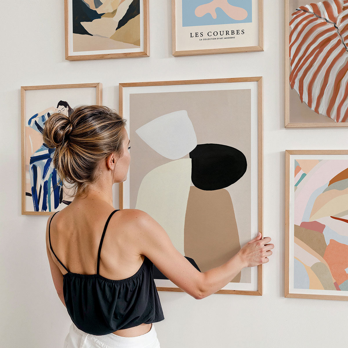 A woman arranging framed artwork prints on a wall.