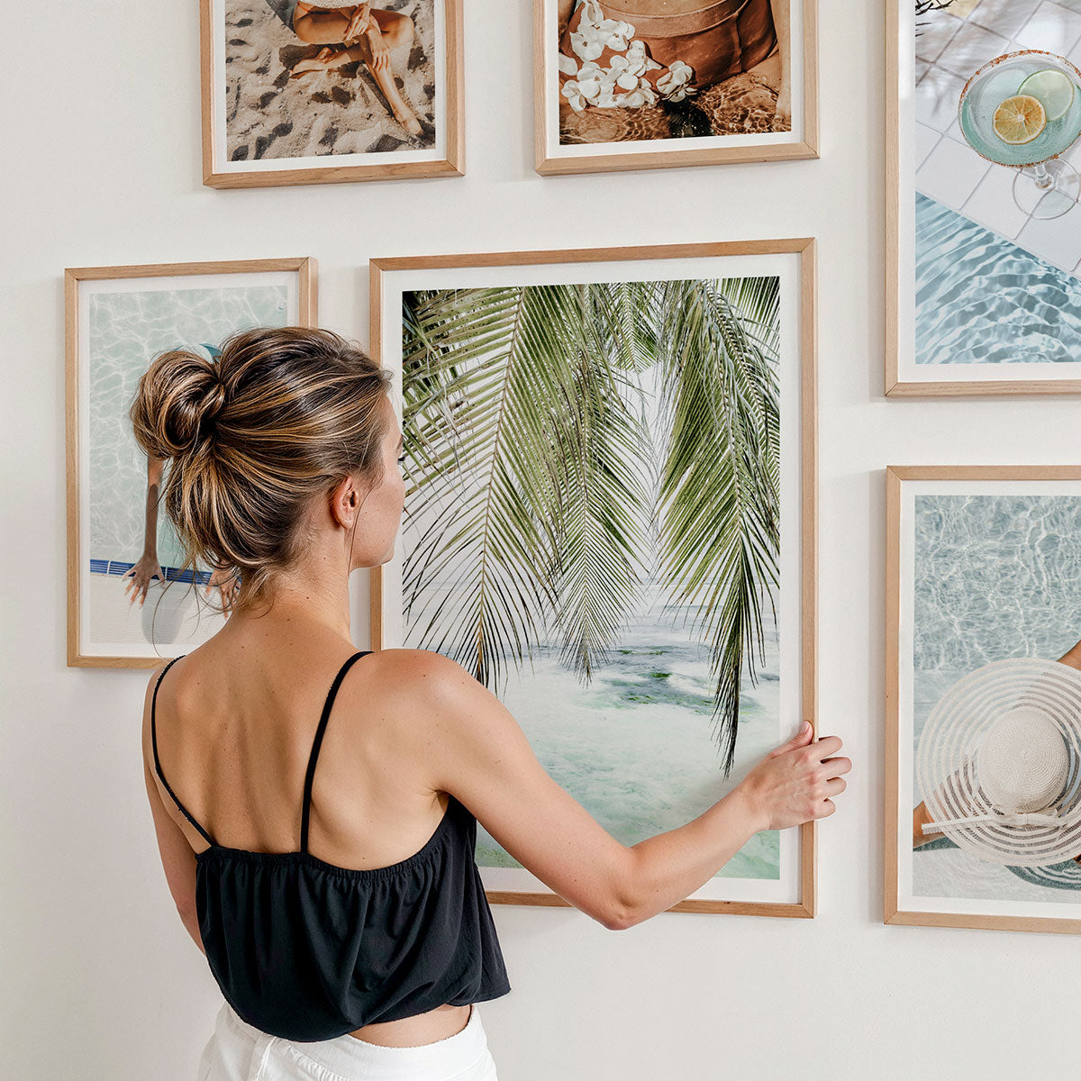 A woman arranging a gallery wall of photographic framed prints. The theme is luxury lifestyle.