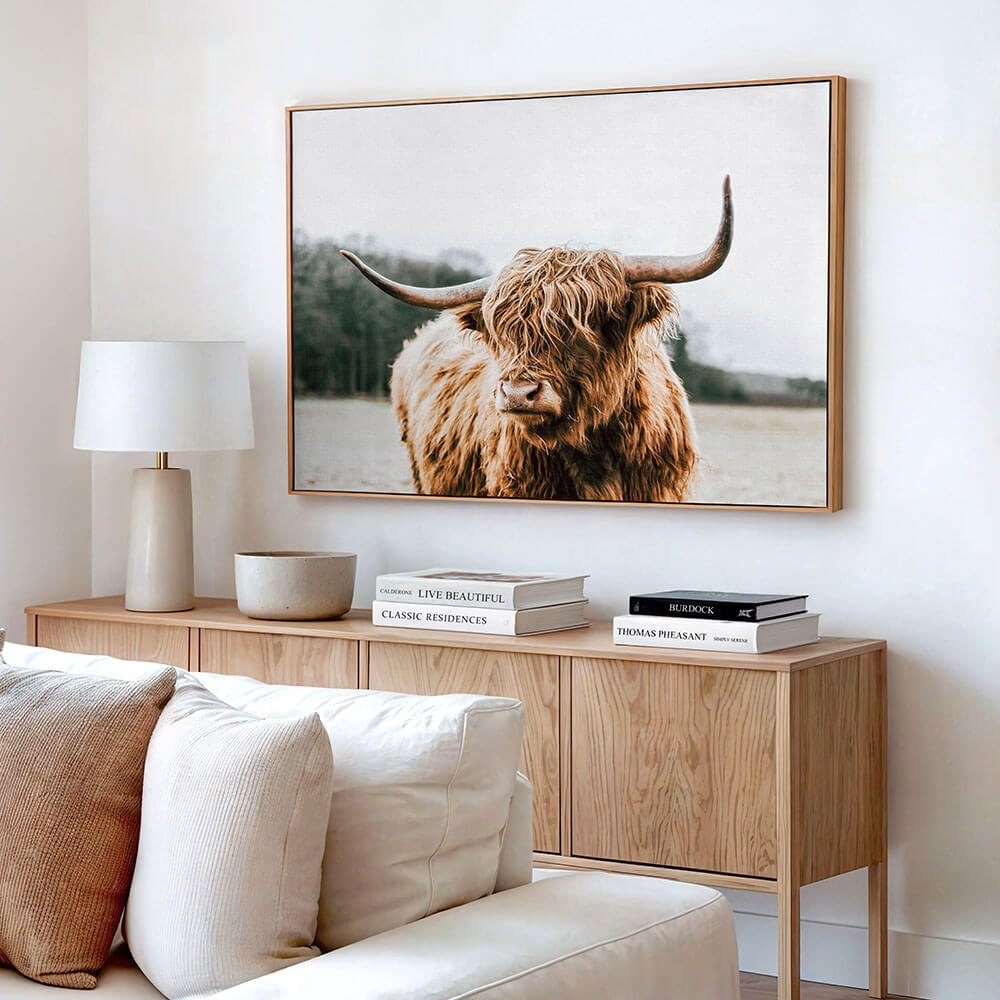A highland cow canvas wall art print in a modern interior with a timber sideboard.