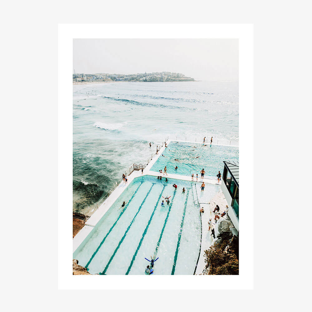 A print of the icebergs pool with a view of the ocean, featuring people swimming and enjoying the water.