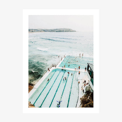 A print of the icebergs pool with a view of the ocean, featuring people swimming and enjoying the water.