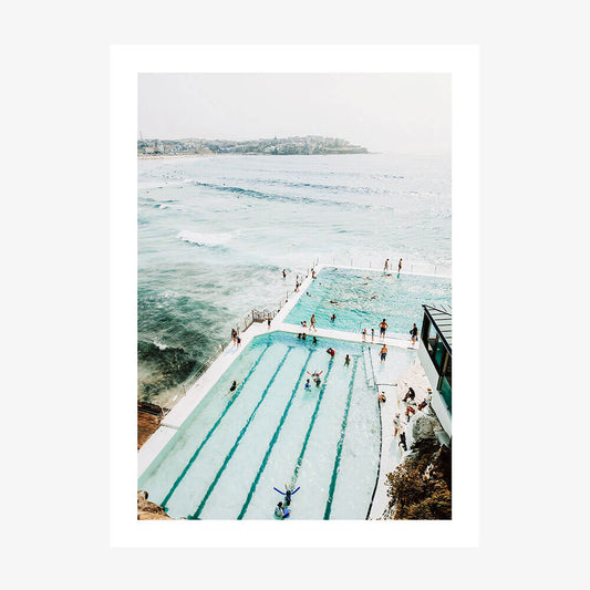A print of the icebergs pool with a view of the ocean, featuring people swimming and enjoying the water.