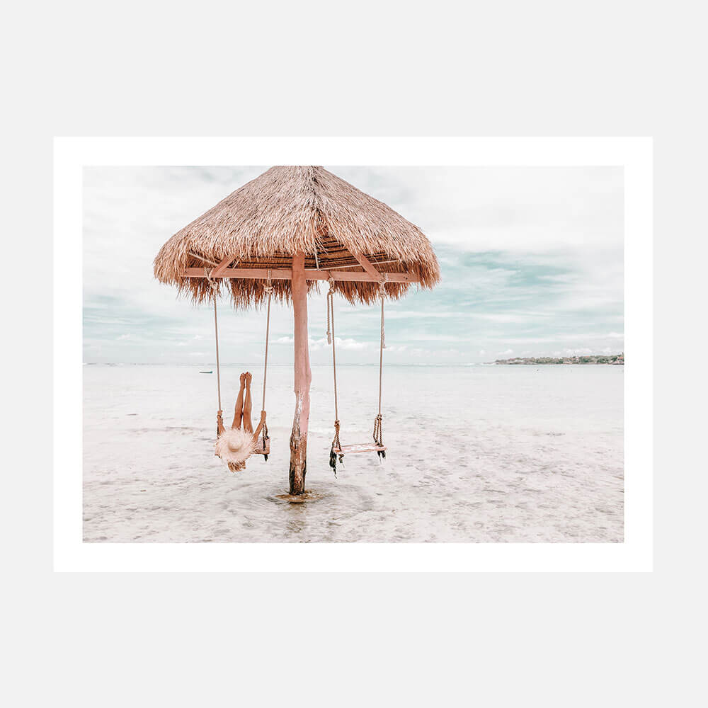 A photo art print featuring a swing hanging from a straw umbrella on a beach, with the ocean in the background.