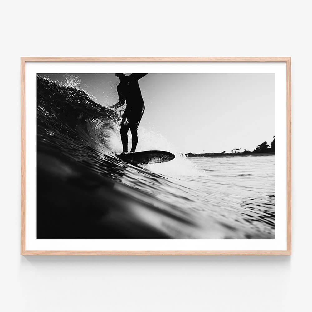 A framed black and white photo wall art print of a surfer on a surfboard, riding a wave in the ocean.