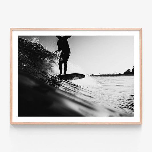 A framed black and white photo wall art print of a surfer on a surfboard, riding a wave in the ocean.
