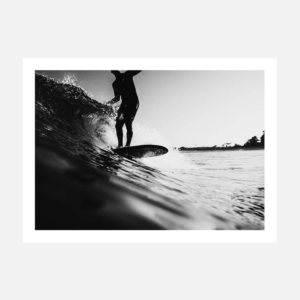 A black and white photo art print of a surfer on a surfboard, riding a wave in the ocean.