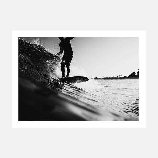 A black and white photo art print of a surfer on a surfboard, riding a wave in the ocean.