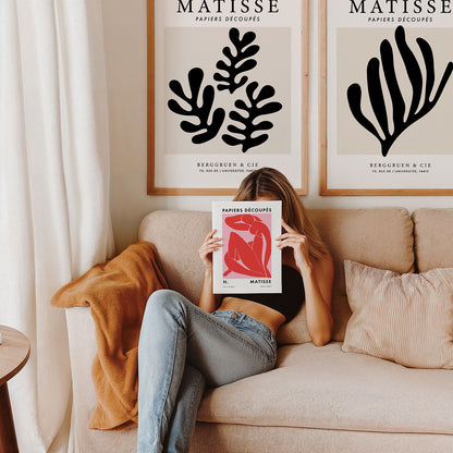 Girl sitting on a couch holding a Matisse poster in front of her face, with two Matisse framed prints on the wall.