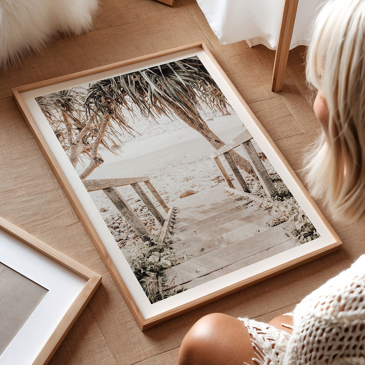 Framed beach photography print on a wooden floor with a person partially visible