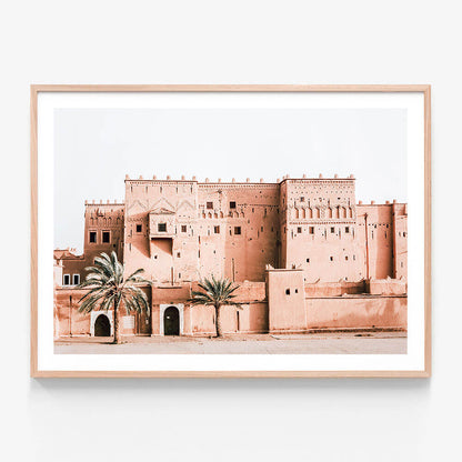 A framed photo print of a Moroccan Kasbah with walls and several gates or openings, surrounded by palm trees.