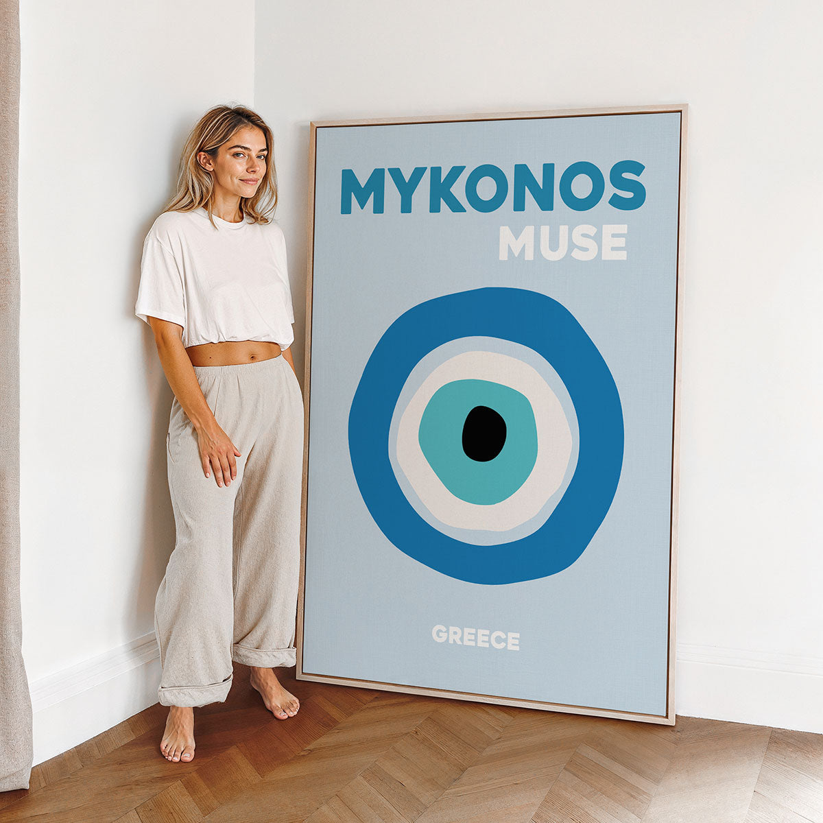Woman standing next to a large framed canvas of a typographic design with the words 'Mykonos Muse' 